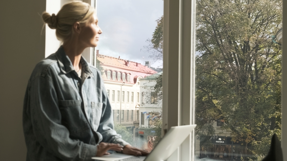 Person sitter i fönster och blickar ut över stan.